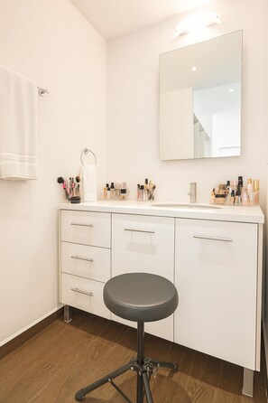 Ein Badezimmer mit weißem Waschtisch, einem Spiegel und einem Hocker.