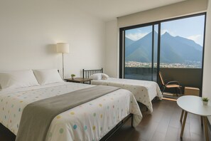 Ett hotellrum med två sängar, ett litet bord, en stol och ett stort fönster med utsikt över bergen.