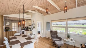 Un intérieur moderne avec un plafond en bois, un coin repas comprenant une table et des chaises, une cuisine et une grande fenêtre offrant une vue dégagée.