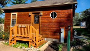 A small wooden cabin with a wooden deck labeled "Pine View," a window, a door, and a satellite dish.