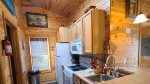 Cocina compacta con armarios de madera, refrigerador, microondas y lavamanos.