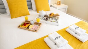 A neatly made bed with a tray of breakfast items, including fruits, pastries, and a beverage. - Villa Tavares Guest Houses (Arouca)