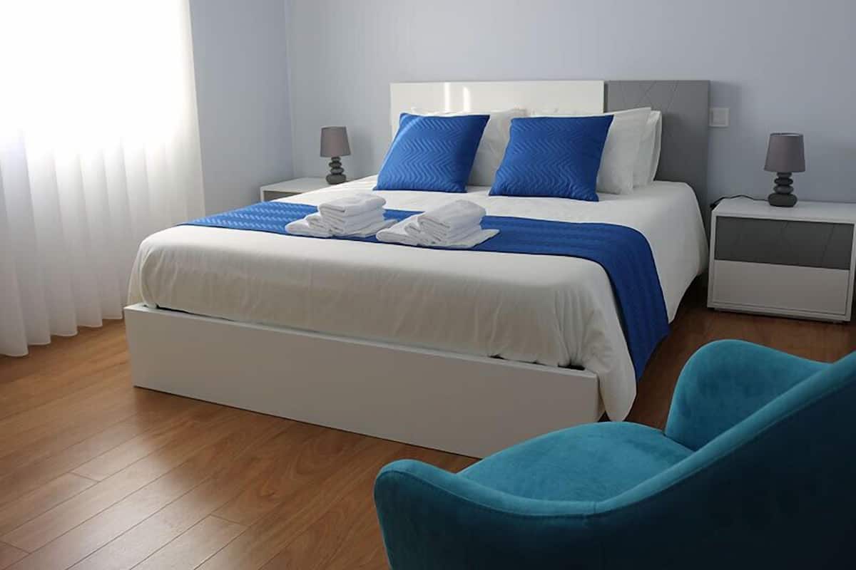 Une chambre d’hôtel avec un lit, deux tables de chevet, une chaise bleue et un plancher en bois.