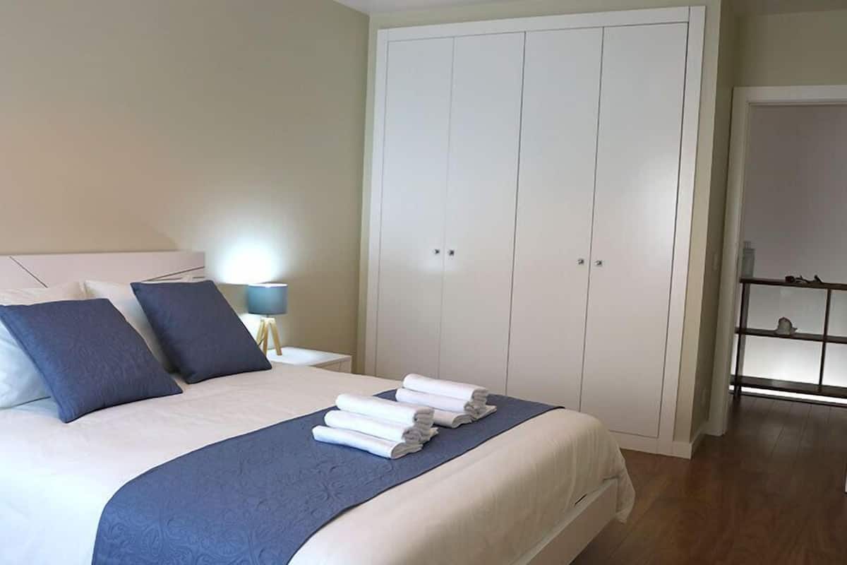 Un lit bien fait, avec une literie bleue et blanche, une lampe de chevet et une armoire à deux portes.