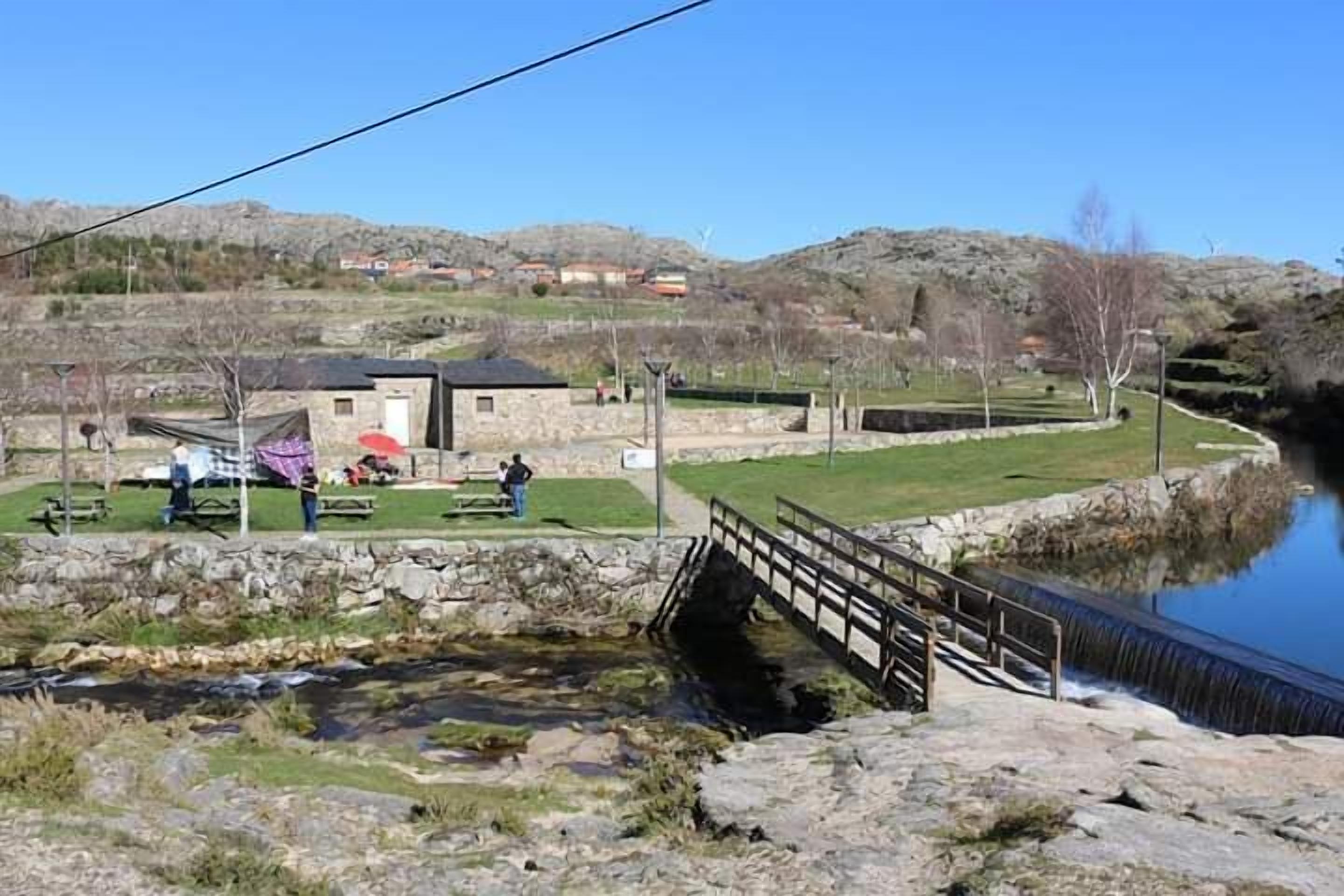 A small stone building with a black roof, a picnic area with tables and chairs, and a wooden bridge over a water channel.