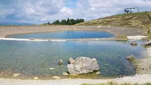 A natural landscape with a clear pond, rocky shore, and a distant mountain range. - Alpine chalet Klippitzzauber (Bad St. Leonhard im Lavanttal)