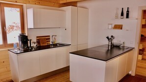 A modern kitchen with white cabinetry, a black countertop, and a built-in oven. There are wine bottles on a shelf above the counter. - Alpine chalet Klippitzzauber (Bad St. Leonhard im Lavanttal)