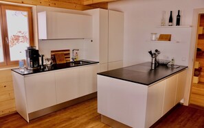 Eine moderne Küche mit weißen Schränken, einer schwarzen Arbeitsplatte und einem eingebauten Backofen. Über der Arbeitsplatte befindet sich ein Regal mit Weinflaschen.