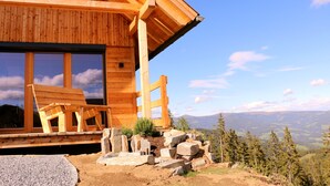 A wooden cabin with large windows, a porch with a bench, and a view of a mountainous landscape. - Alpine chalet Klippitzzauber (Bad St. Leonhard im Lavanttal)