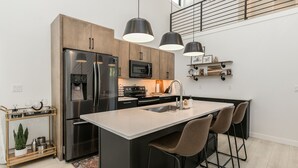Una cocina moderna con una isla central, electrodomésticos de acero inoxidable, iluminación colgante y vistas al piso superior.