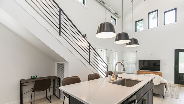 Una cocina moderna con una isla central, un comedor con sillas, una escalera y un amplio ventanal que proporciona luz natural.