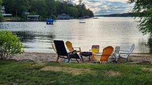 Une vue sur le lac, avec des chaises et une table sur la rive, des bateaux sur l’eau et des maisons en arrière-plan.