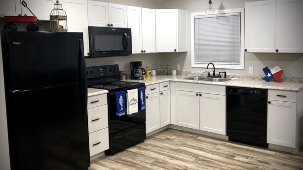 A modern kitchen with white cabinets, a black refrigerator, a microwave, a stove, and a dishwasher.