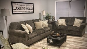 A living room with two dark brown sofas, patterned chairs, a coffee table, and a framed sign on the wall.