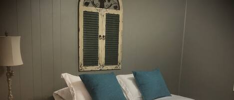 A bedroom with a bed, a nightstand, a lamp, and a window with shutters.