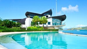 Un edificio moderno con un techo curvo singular, una piscina y vistas al mar.