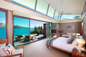 A modern hotel room with a large bed, a television, and a balcony with a view of the sea.