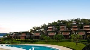 Un hotel moderno con varios pisos, piscina y abundante vegetación.
