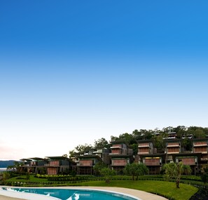 A modern hotel with multiple floors, a swimming pool, and lush landscaping. - Yacht Club Villas (Whitsundays)