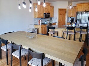 Eine moderne Küche mit Holzschränken, einem Edelstahlkühlschrank und einem Essbereich mit großem Tisch und Stühlen.
