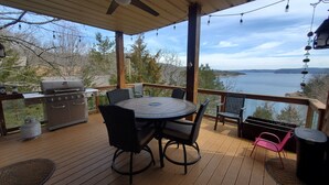 A covered outdoor deck with a round table and chairs, a grill, and a view of a lake. - Camp Roberts-Lakefront-8 Bedrooms-Sleeps 19-Big; Lake View-Community Pool! (Garfield)