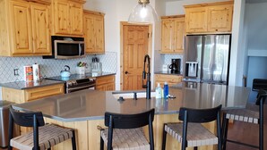 A modern kitchen with wooden cabinets, stainless steel appliances, and a central island with bar stools. - Camp Roberts-Lakefront-8 Bedrooms-Sleeps 19-Big; Lake View-Community Pool! (Garfield)
