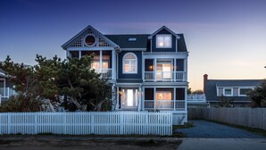 Une maison à deux étages, avec une clôture en bois peinte en blanc, de nombreuses fenêtres et une véranda.