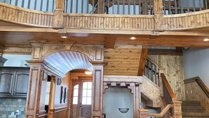 En rummelig opholdsstue med højt til loftet, en trætrappe og en balkon med gelænder.