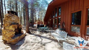 Une cabane dotée d’une cheminée en pierre, d’un espace salon extérieur et de grandes fenêtres.