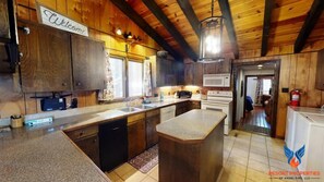A spacious kitchen with wooden cabinets, a large island, and a welcoming sign.