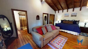 A cozy room with a wooden floor, a sofa with cushions, a bed with a blue bedspread, and a mirror on the wall.