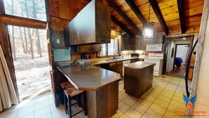 A rustic kitchen with wooden cabinets, a large island, and a view of the forest. - Close to Country Club | Fireplace | Single Level | Happy Pines (Angel Fire)