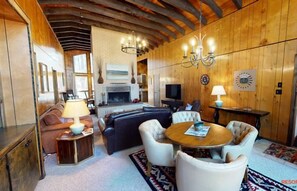 A cozy living room with a fireplace, a dining area with a round table, and a kitchen in the background.