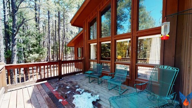 Une terrasse en bois avec des chaises et une table en verre, entourée de grandes fenêtres et offrant une vue sur les arbres.