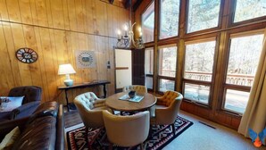 Une pièce chaleureuse avec un décor intérieur en bois, une table ronde entourée de chaises, une lampe et une horloge au mur.