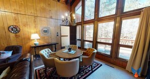 A cozy room with a wooden interior, a round table with chairs, a lamp, and a clock on the wall.