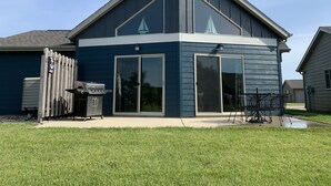 A modern house with a large sliding glass door, a covered patio, and a visible grill area. - Relax and make fun memories in our Vacation Home at Bridges Bay Resort (Arnolds Park)