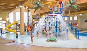 Ein Indoor-Wasserpark mit zentralem Wasserspiel, Rutschen und einem Poolbereich.