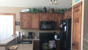A kitchen with wooden cabinets, a black refrigerator, a microwave, and a stove. - Relax and make fun memories in our Vacation Home at Bridges Bay Resort (Arnolds Park)