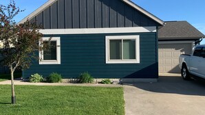 A two-story house with a dark green exterior and white trim, a garage, and a driveway with a parked car. - Relax and make fun memories in our Vacation Home at Bridges Bay Resort (Arnolds Park)