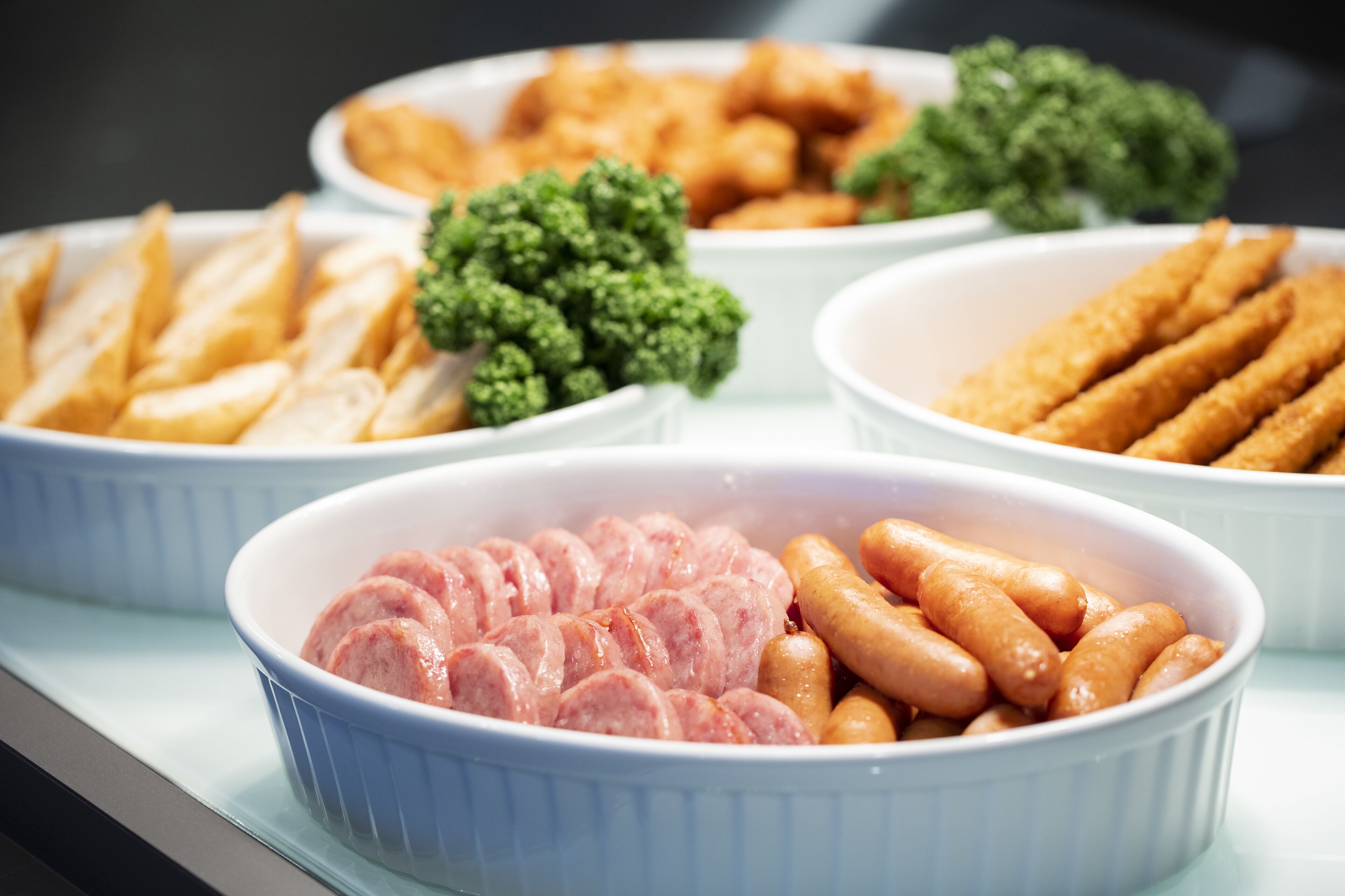 A buffet with various dishes including sausages, fries, and vegetables.