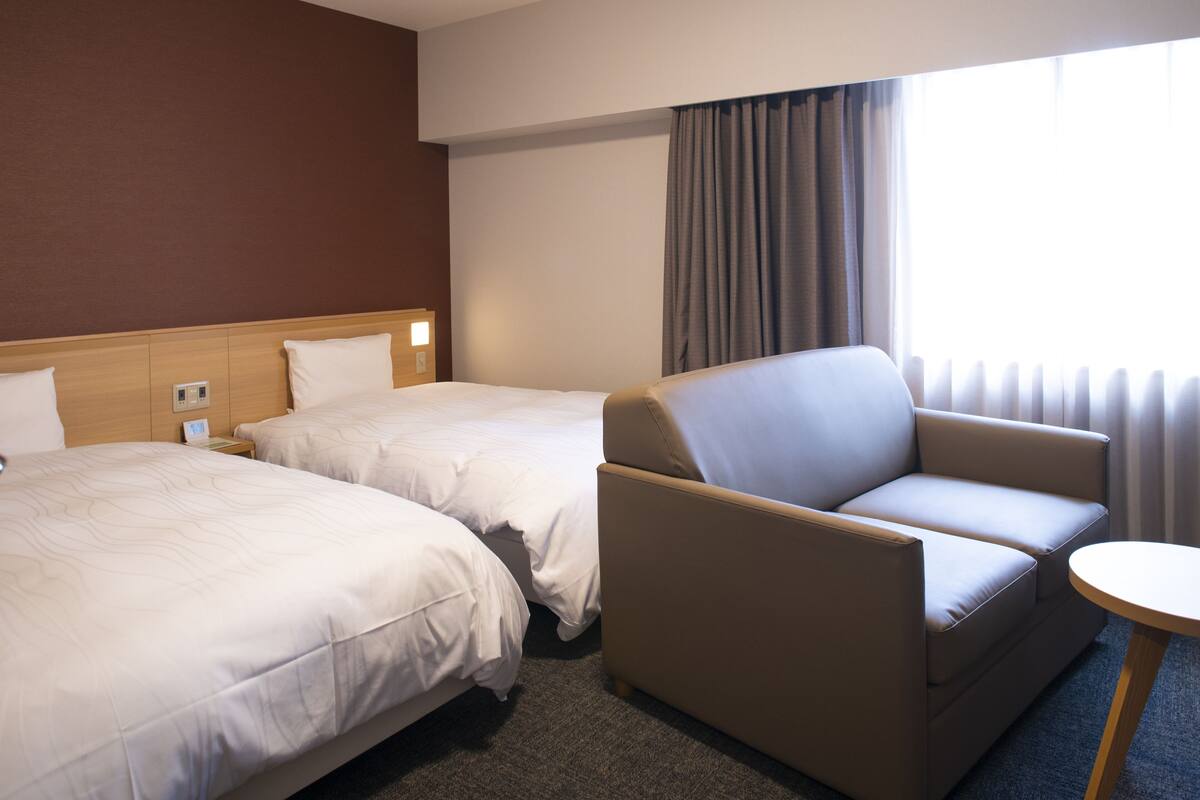 A hotel room with two beds, a sofa, and a small table.