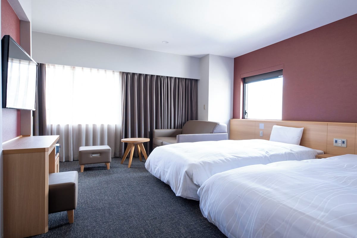 A hotel room with two beds, a desk, a chair, and a small table.