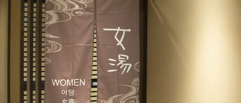 Una habitación con una cortina que muestra texto en varios idiomas y un letrero que señala la sección de mujeres.