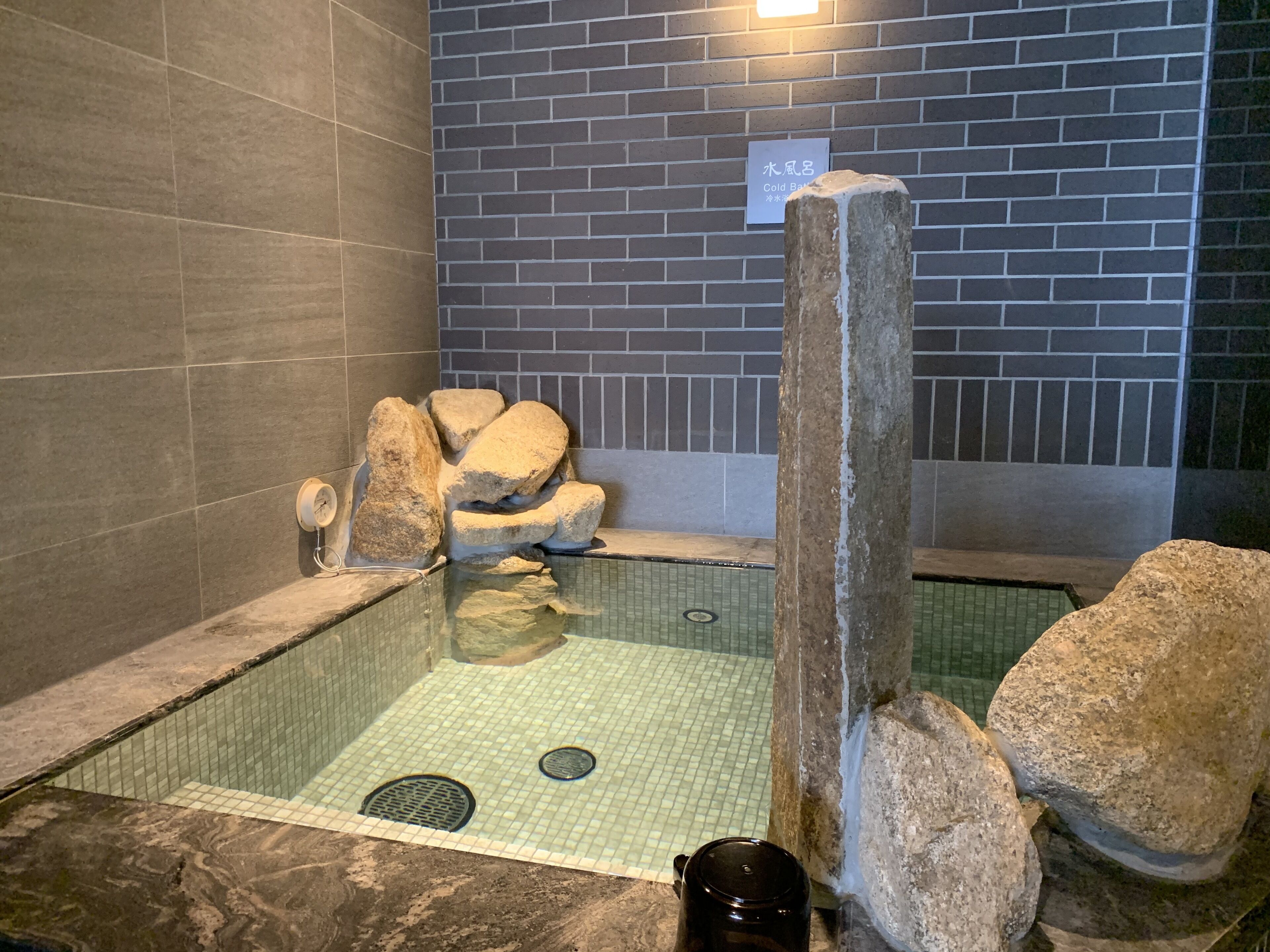 Un bain à remous en pierre, avec un sol carrelé et un mur en briques en arrière-plan.