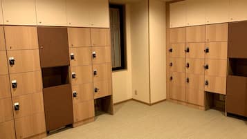 A row of wooden lockers with numbered compartments, carpeted floor, and a window with blinds.