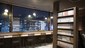 A library with bookshelves and a view of a cityscape through a large window. - Dormy Inn Nagasakiekimae Hot Springs (Nagasaki)