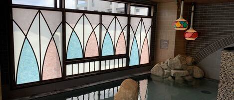 Una habitación con un amplio ventanal con vidrieras, una pared de piedra y un pequeño elemento acuático interior.