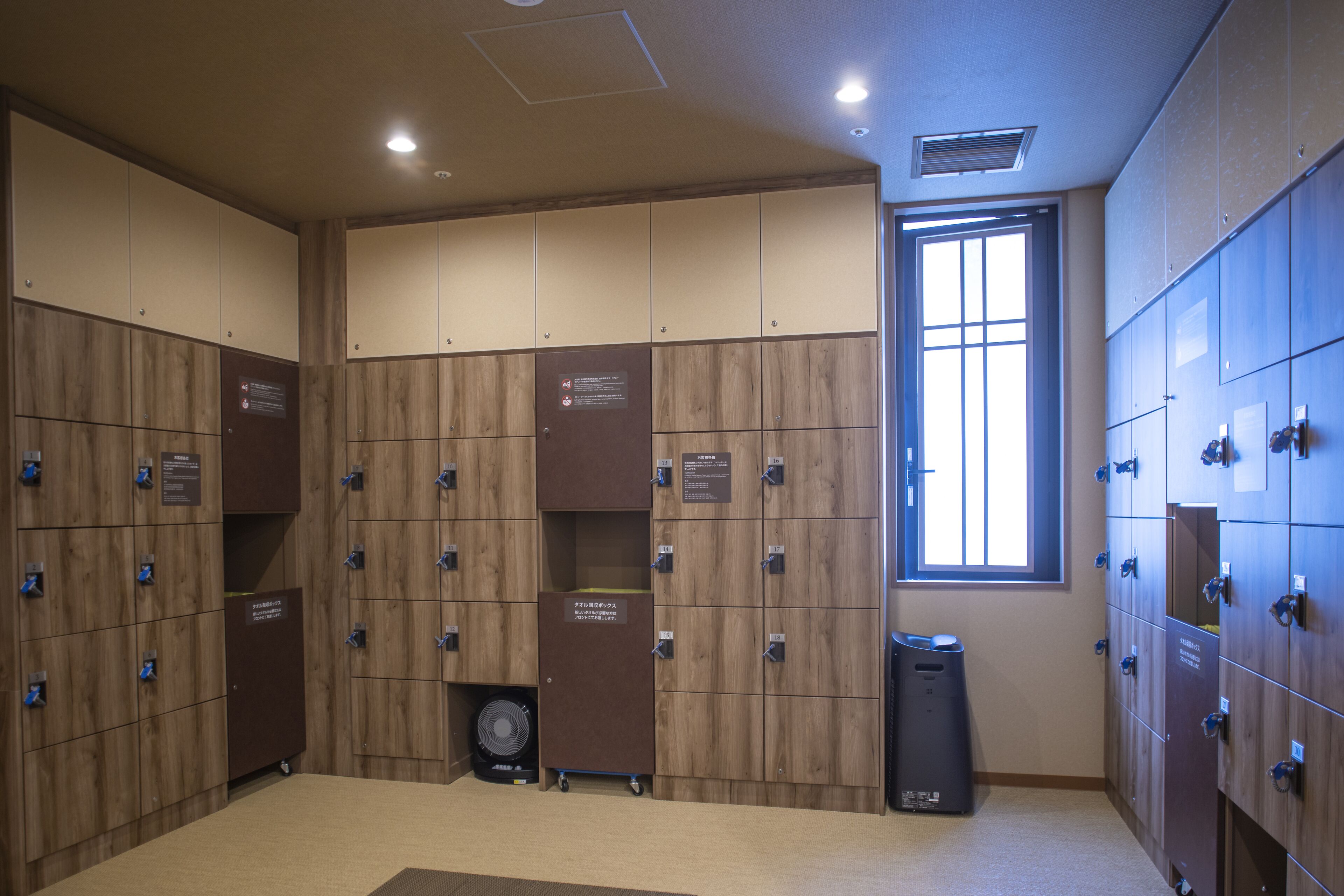 A locker room with multiple lockers, a window, and a trash bin.