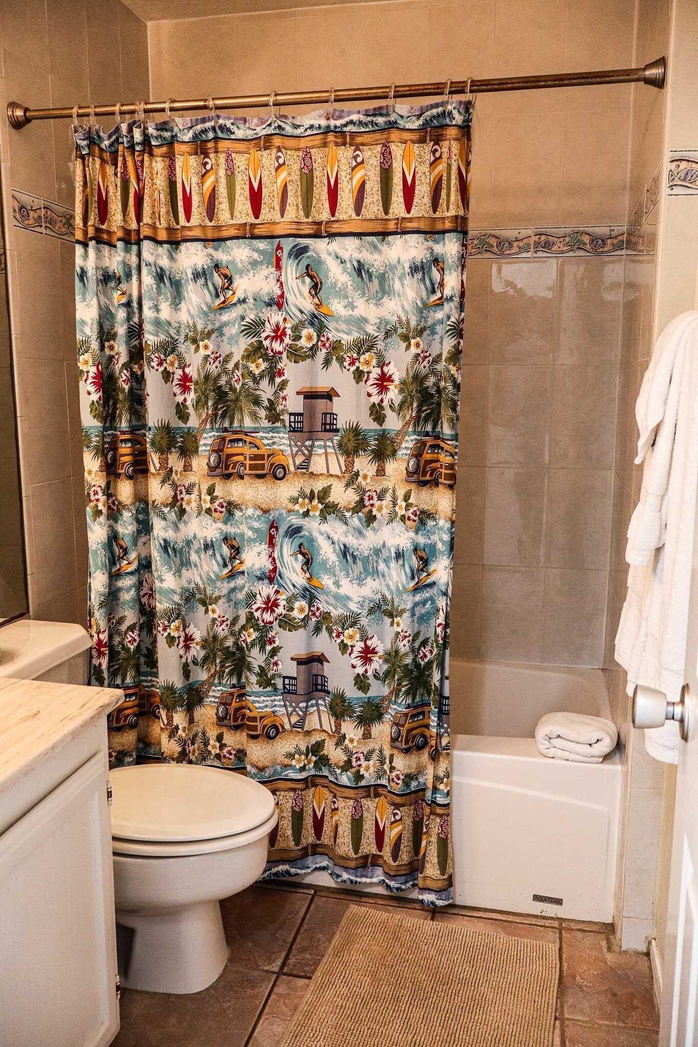 A bathroom with a shower curtain featuring a tropical design, a toilet, a bathtub, and a towel rack.